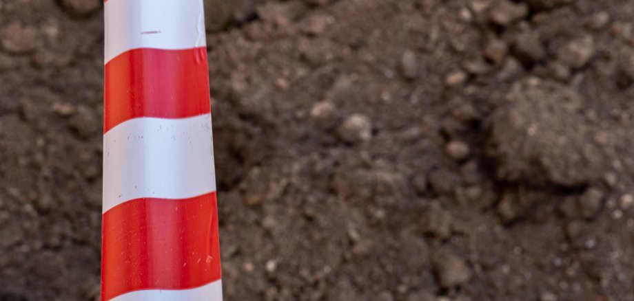 Red and white barrier tape protect a danger place. The warning tape indicates the danger of being on the territory of the construction site. Dug trenches for laying new pipes.